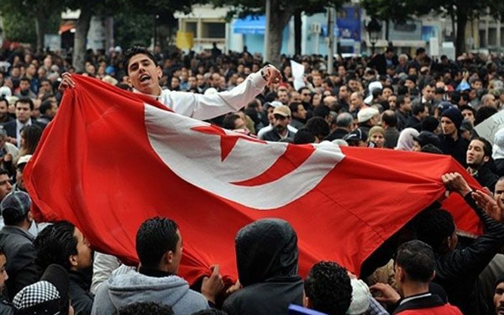 Туніс. Учасник акції протесту в Тунісі тримає національний прапор під час антиурядової демонстрації на проспекті Хабіб Бургиба. Сотні людей, які брали участь у першому мітингу на підтримку нового тимчасового уряду Тунісу, були розігнані іншими демонстрантами, що вимагали відставки уряду. / © AFP