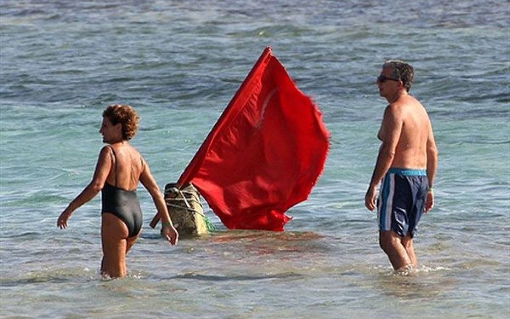 Єгипет, Шарм Ель-Шейх. Туристи проходять повз червоний прапор-попередження, який вивісили, оскільки на пляжі курорта Шарм-еш-Шейх, розташованого на Червоному морі, знову були помічені акули. Цього року вже сталося кілька нападів акул на людей. / © AFP