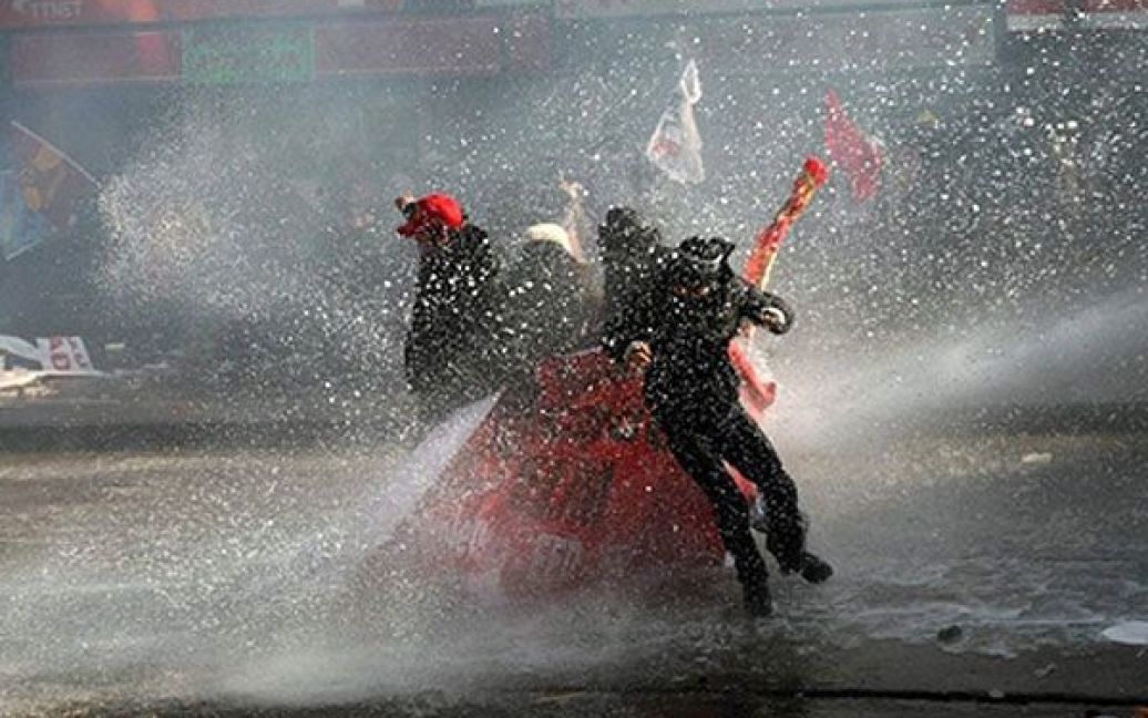 Туреччина, Анкара. Демонстранти намагаються захистити себе плакатами від водометів, які поліція використала для розгону акції протесту в Анкарі. Поліція використала сльозогінний газ і водомети для розгону тисяч робітників, які вийшли на вулиці на знак протесту проти спірного законопроекту про трудові права. / © AFP