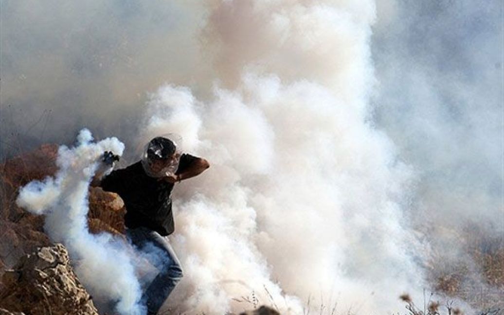 Нілін. Палестинський демонстрант, захищаючи голову поліетиленовим пакетом, готується кинути назад сльозогінну бомбу, випущену ізраїльськими військовими у демонстрантів, під час щотижневої акції протесту проти спірного розділового бар&#039;єру. / © AFP