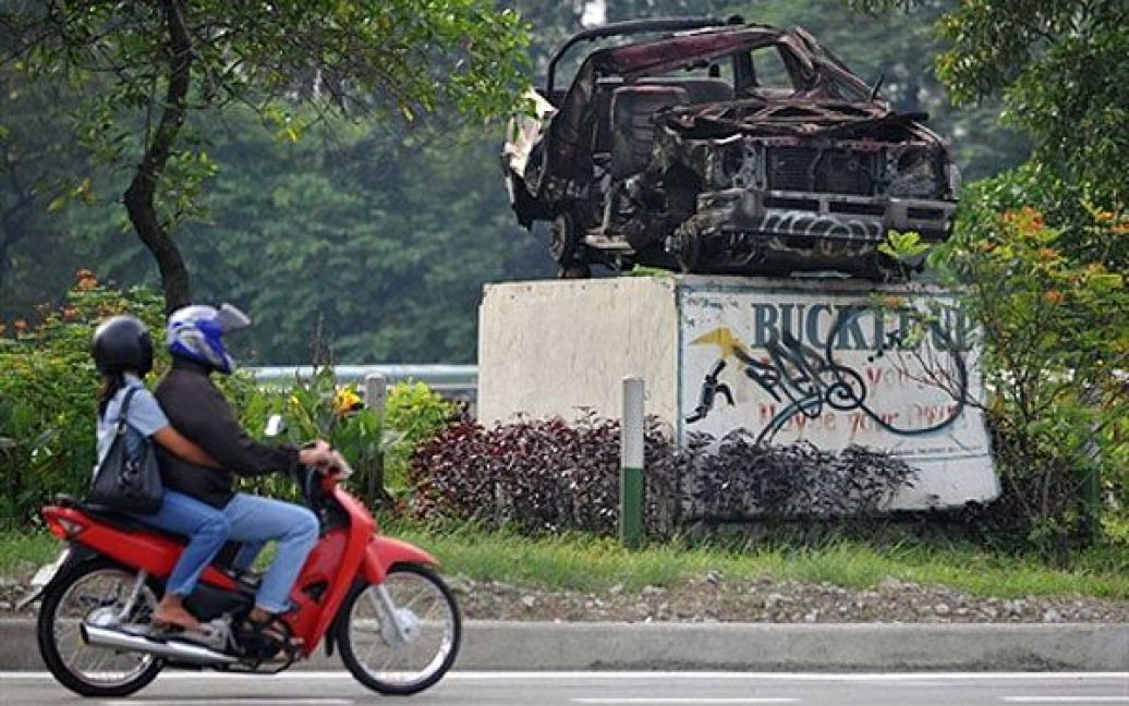 Філіппіни, Маніла. Люди проїздять повз розбитий автомобіль, виставлений як попередження для водіїв. Напис поруч з автомобілем: "Пристебнись. Життя, яке ти рятуєш, може бути твоїм власним". / © AFP