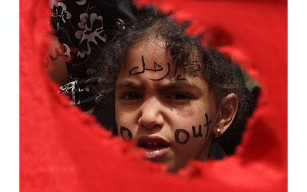 Ємен, Сана. Дівчинка виглядає крізь отвір у національному прапорі Ємену під час антиурядової демонстрації, учасники якої вимагали відставки президента Ємену Алі Абдалли Салеха. / © AFP