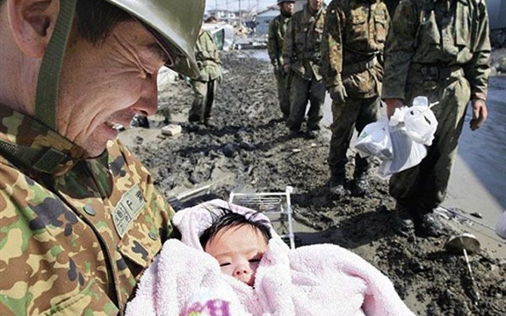 Японія, Ісіномакі. Солдат самооборони тримає на руках чотиримісячну дитину, яка вижила після руйнівного цунамі у місті Ісіномакі, префектура Міягі. Кількість жертв руйнівного землетрусу та цунамі в Японії перевищило 10 тисяч осіб. / © AFP