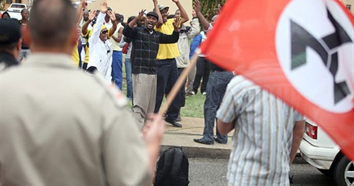 Південна Африка, Вентерсдорп. Члени правлячого Африканського національного конгресу співають під час зіткнення з прихильниками крайньо правої політичної організації і колишньої воєнізованої групи Африканерський руху опору (АРО). Групи зустрілись біля будівлі суду в місті Вентерсдорп, де почався судовий процес над 15-річним неповнолітнім, якому були пред'явлені звинувачення у забитті до смерті 69-річного лідера АРО Євгена Терібланша. Терібланш був забитий до смерті у своєму ліжку в квітні. Це вбивство потрясло країну, в якій досі зберігається расова напруженість через 16 років після закінчення апартеїду. / © AFP