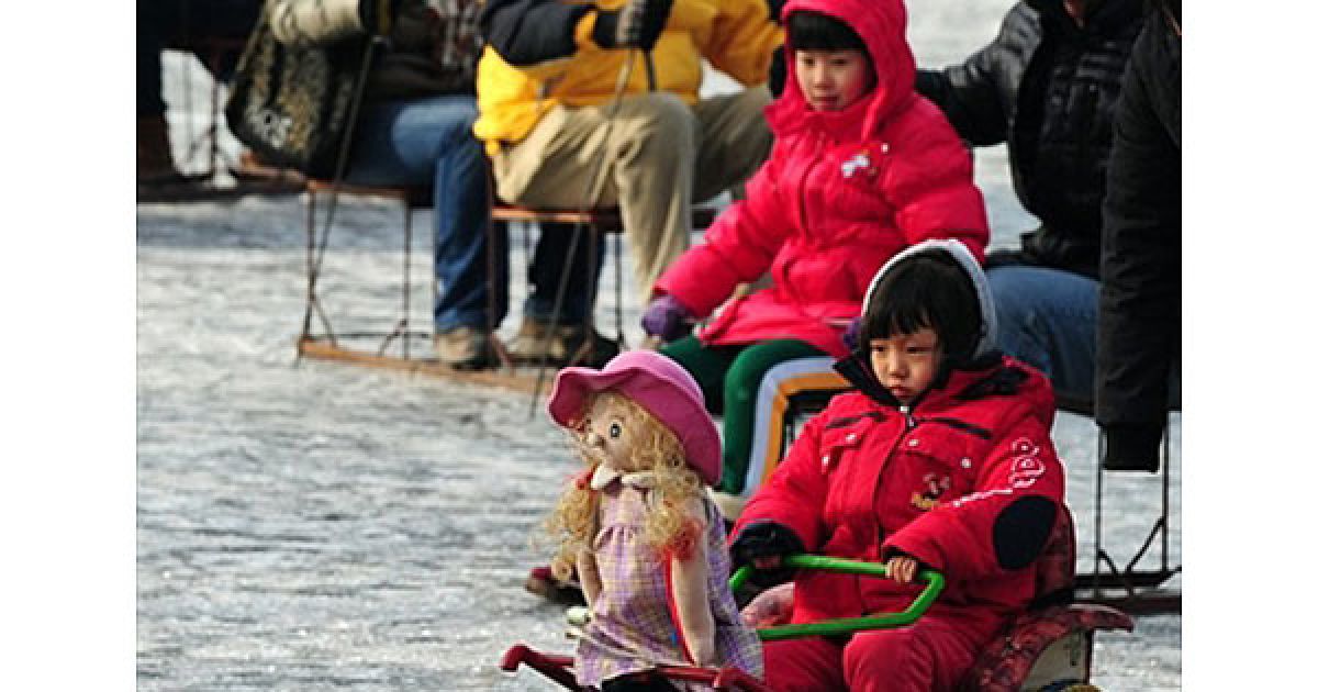 Китай, Пекін. Молода дівчина катається на візку, який тягне механічна лялька, на замерзлому озері на біля башти Драм у центрі Пекіна. / © AFP