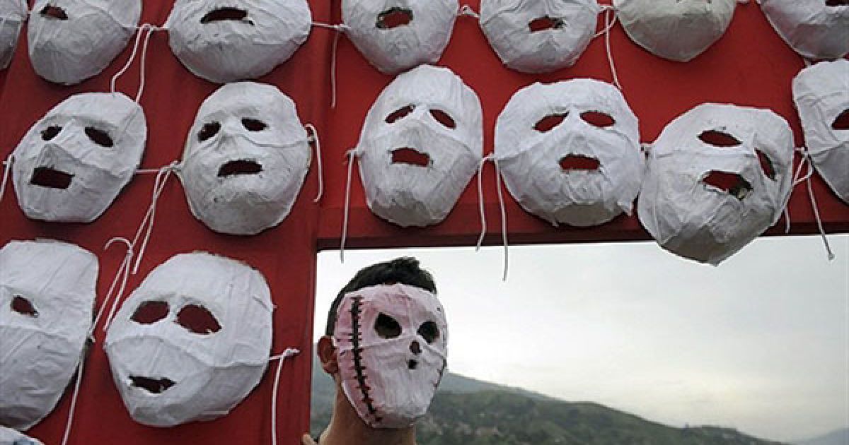 Колумбія, Медельїн. Людина у масці тримає хрест на Ла Ескомбрера, звалищі для будівельних матеріалів, на околиці Медельїну, департамент Антіокия, Колумбія. За словами місцевих жителів, близько 160 чоловік були вбиті і поховані воєнізованими колумбійськими партизанами на цьому звалищі. / © AFP