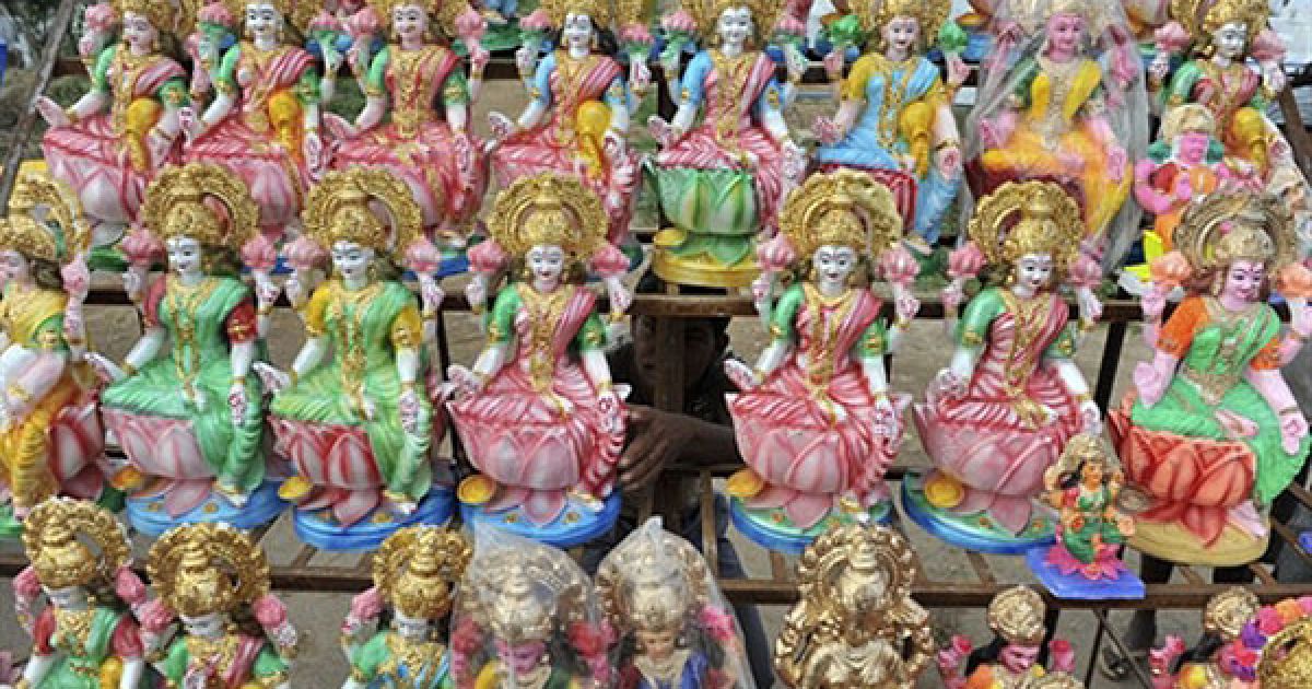 Індія, Хайдарабад. Індійський працівник поправляє статуї індуїстської богині Лакшмі, яка символізує гроші та багатство, виставлені у придорожньому кіоску в Хайдарабаді. В Індії відзначають свято вогнів Дівалі. / © AFP