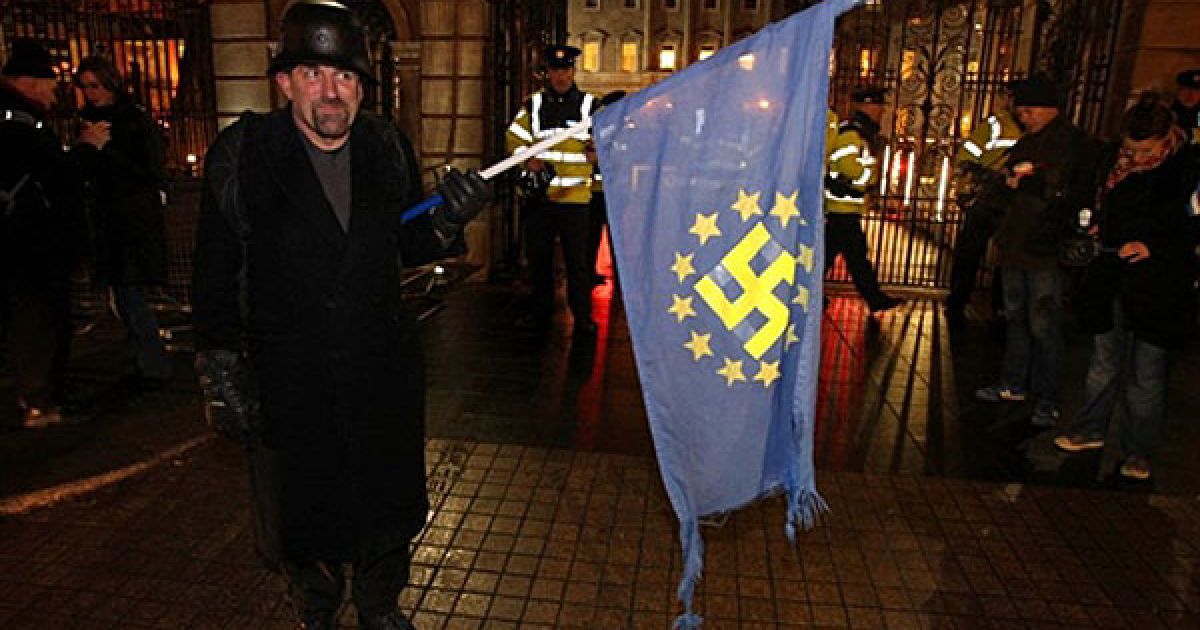 Ірландія, Дублін. Демонстрант тримає прапор ЄС зі свастикою в центрі під час акції протесту перед будівлею ірландського парламенту в Дубліні. Парламент Ірландії проголосував за отримання 85 млрд євро допомоги від ЄС та МВФ. Міністр фінансів Ірландії Браян Леніхан заявив, що це єдиний варіант для відновлення зруйнованої ірландської економіки. / © AFP