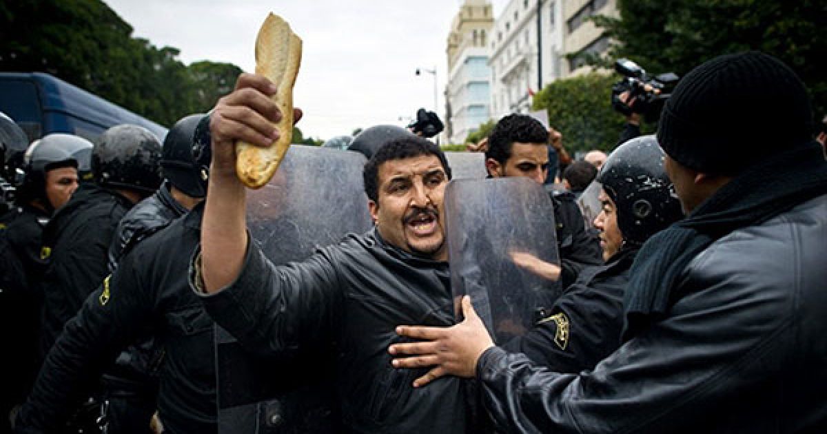 Туніс. Туніського демонстранта, який тримає в руці хліб під час акції протесту в Тунісі, зупиняють співробітники ОМОНу. Поліція застосувала сльозогінний газ для розгону антиурядової демонстрації в центрі столиці, в якій взяли участь кілька сотень людей. / © AFP