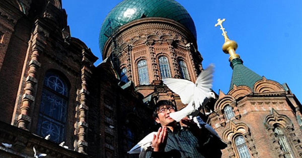 Китай, Харбін. Людина годує голубів перед Софійським собором у Харбіні. Собор був побудований у 1907 році після завершення Транс-Сибірської залізниці. / © AFP
