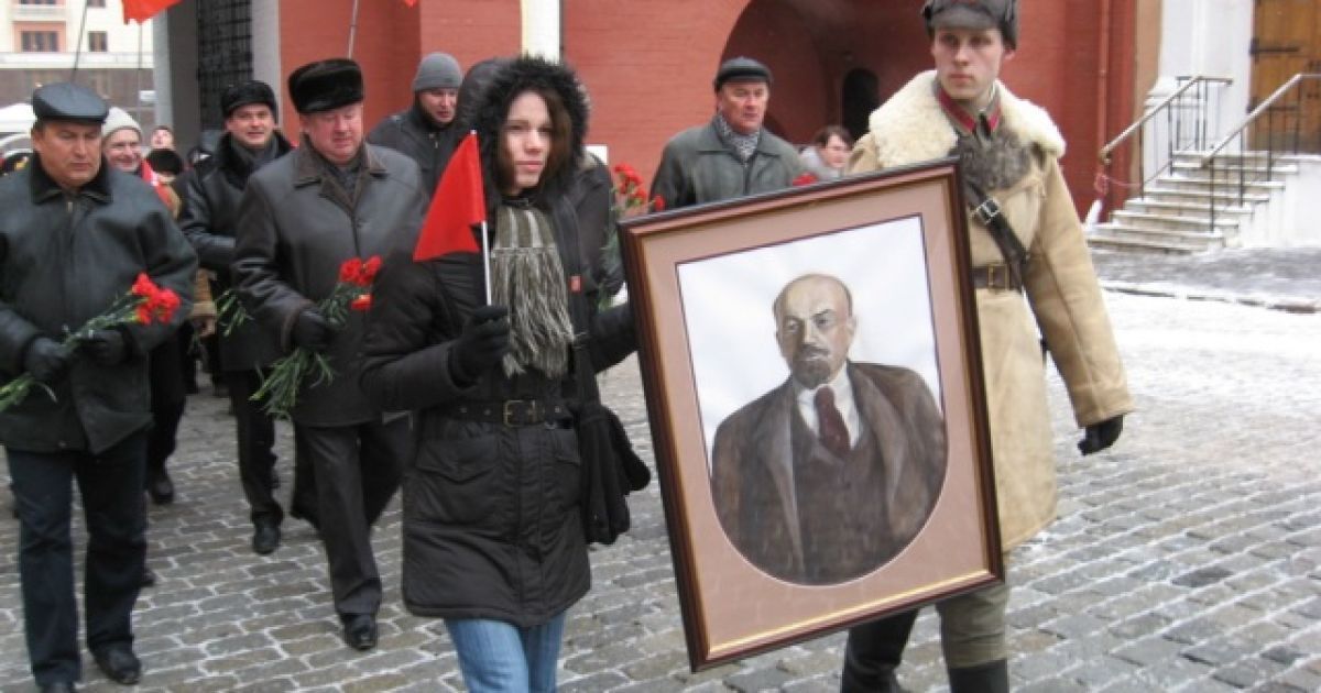 Молода дівчина в шарфі з символікою КПРФ і юнак у будьонівці несли портрет Володимира Леніна.