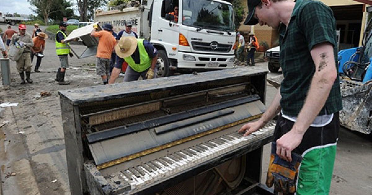 Австралія, Брісбен. Доброволець грає на пошкодженому водою фортепіано під час операції з розчищення зруйнованого повінню будинку у передмісті міста Брісбен. / © AFP