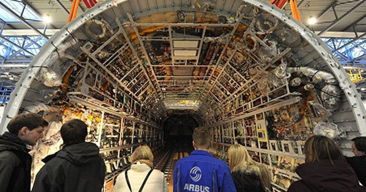 Німеччина, Бремен. Співробітники компанії "Airbus" стоять перед фюзеляжем нового літака, виробленого на заводі у Бремені. Модуль був побудований як частина п'ятого прототипа літака "Airbus A400M", його первезуть до Севільї (Іспанія), де відбувається остаточне збирання винищувачів. / © AFP