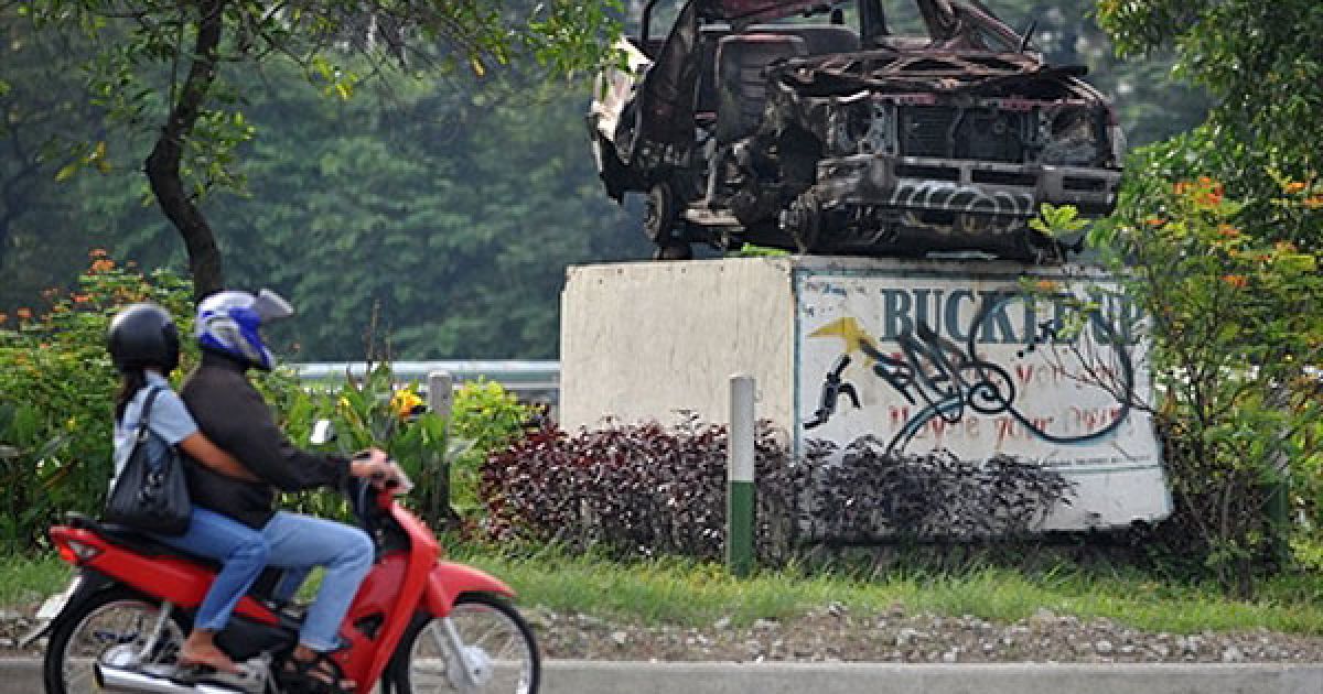Філіппіни, Маніла. Люди проїздять повз розбитий автомобіль, виставлений як попередження для водіїв. Напис поруч з автомобілем: "Пристебнись. Життя, яке ти рятуєш, може бути твоїм власним". / © AFP