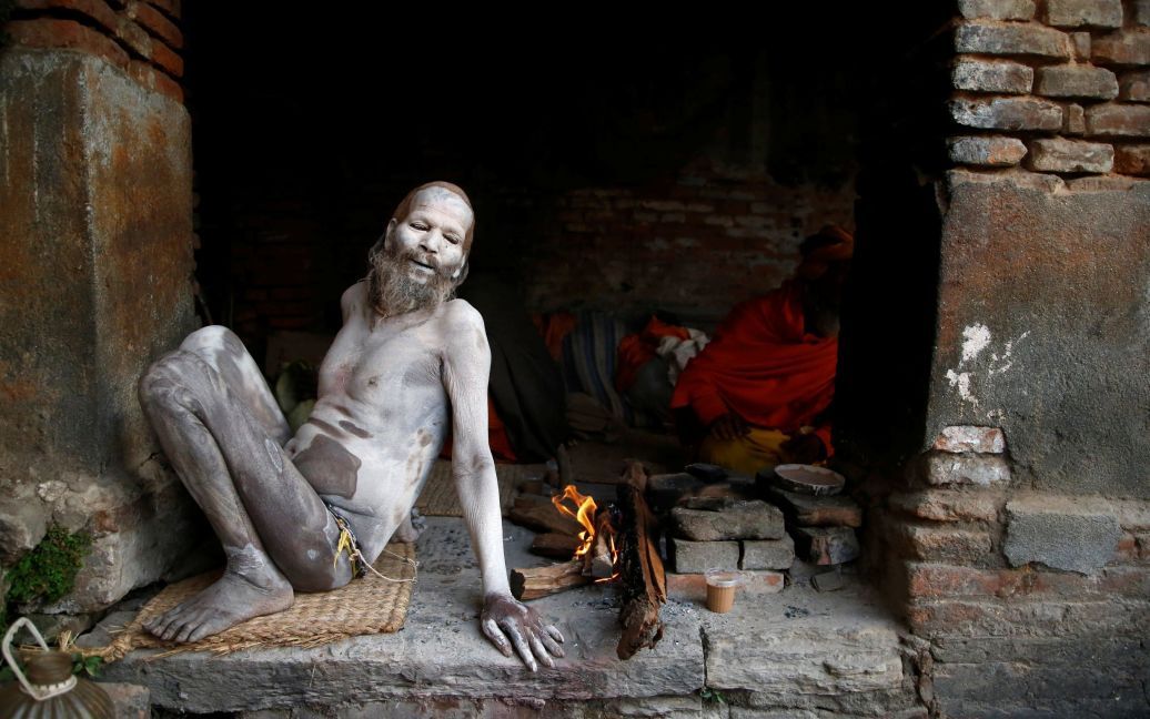 Садху, или индуистский святой, сидит рядом с огнем после того, как его тело размазали золой в помещении храма Пашупатинат, накануне праздника Шиваратри в Катманду, Непал. / © Reuters