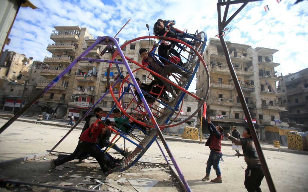 Діти катаються на гойдалках в пошкодженому обстрілами районі в Алеппо, Сирія. / © Reuters