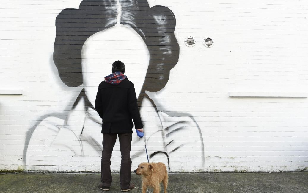 Человек и его собака остановились, чтобы посмотреть на граффити, изображающий принцессу Лею из фильма &ldquo;Звездные войны&rdquo;, которую играет Кэрри Фишер (Белфаст, Северная Ирландия). / © Reuters