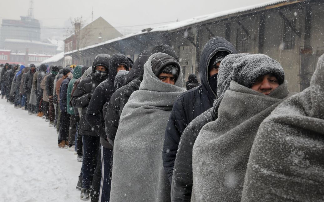Мигранты ждут в очереди на тарелку бесплатной еды во время снегопада за пределами заброшенного таможенного склада в Белграде, Сербия. / © Reuters