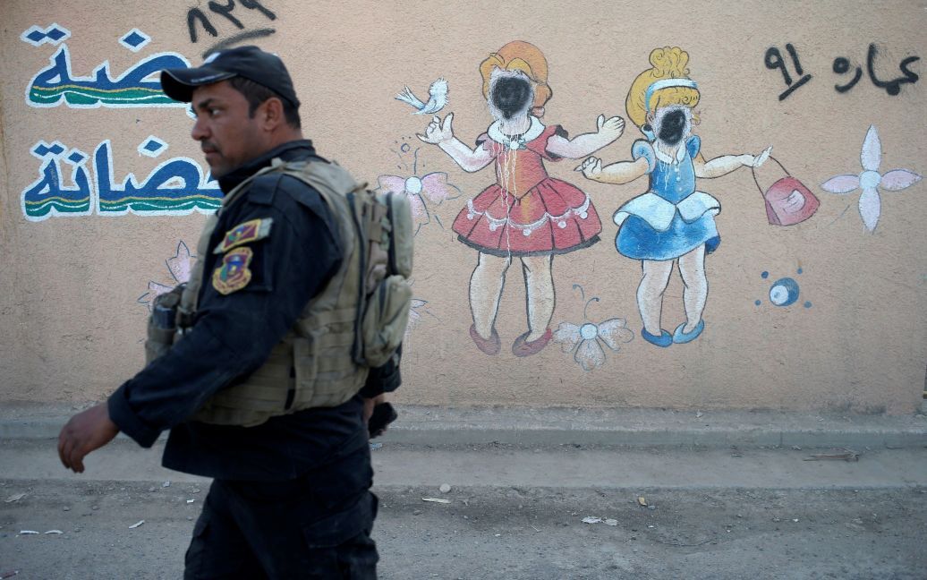 Боєць іракського спецпризначення проходить повз мурал з намальованими дітьми, обличчя яких зафарбували бойовики &ldquo;ІД&rdquo;, на стіні дитячого садочка у Мосулі, Ірак. / © Reuters