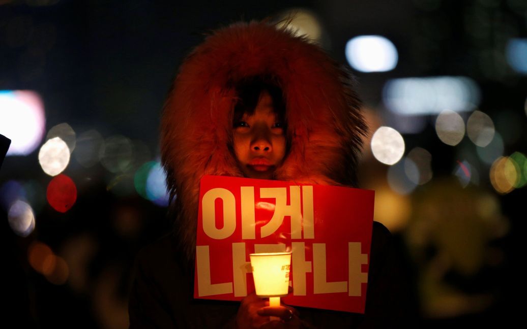Женщина держит свечу и транспарант на акции протеста в Сеуле, призывая президента Южной Кореи Пак Кын Хе уйти в отставку. Президента обвиняют в коррупции. / © Reuters