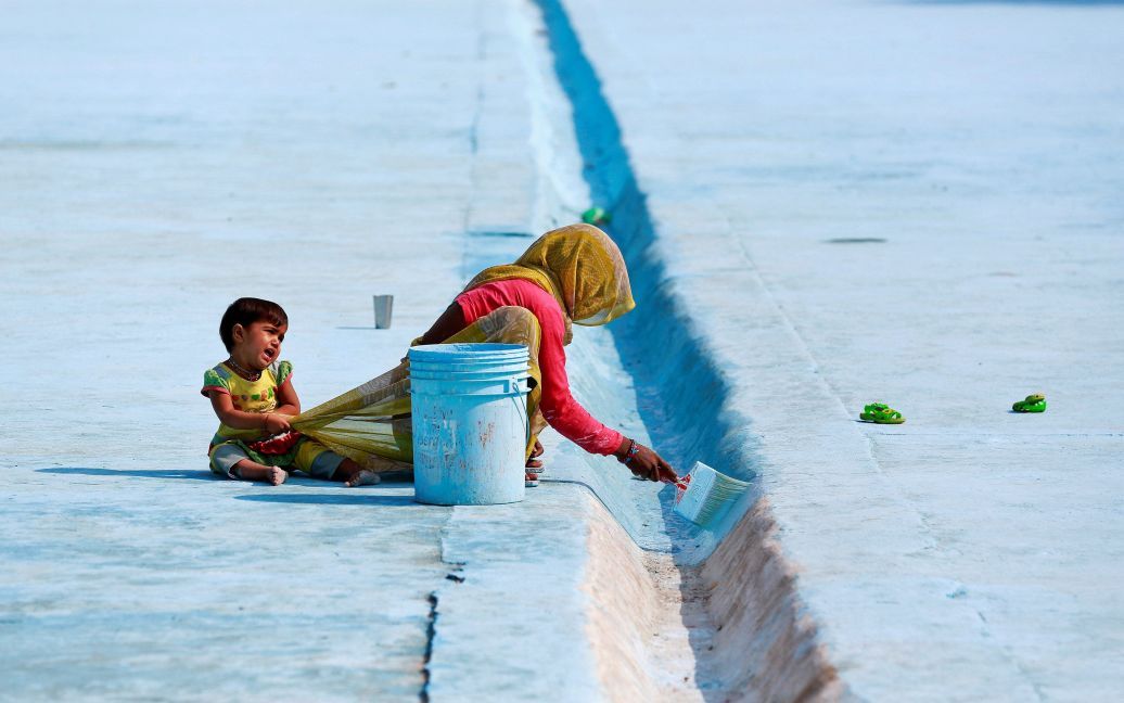 Жінка фарбує підлогу ставка, у той час як її дитина тягне за її сарі в Делі, Індія. / © Reuters