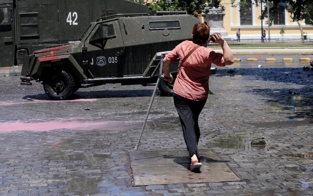 Жінка за допомогою милиці готується кинути камінь у бік броньованої машини спецпризначенців під час страйку проти національної пенсійної системи в Сантьяго, Чилі. / © Reuters