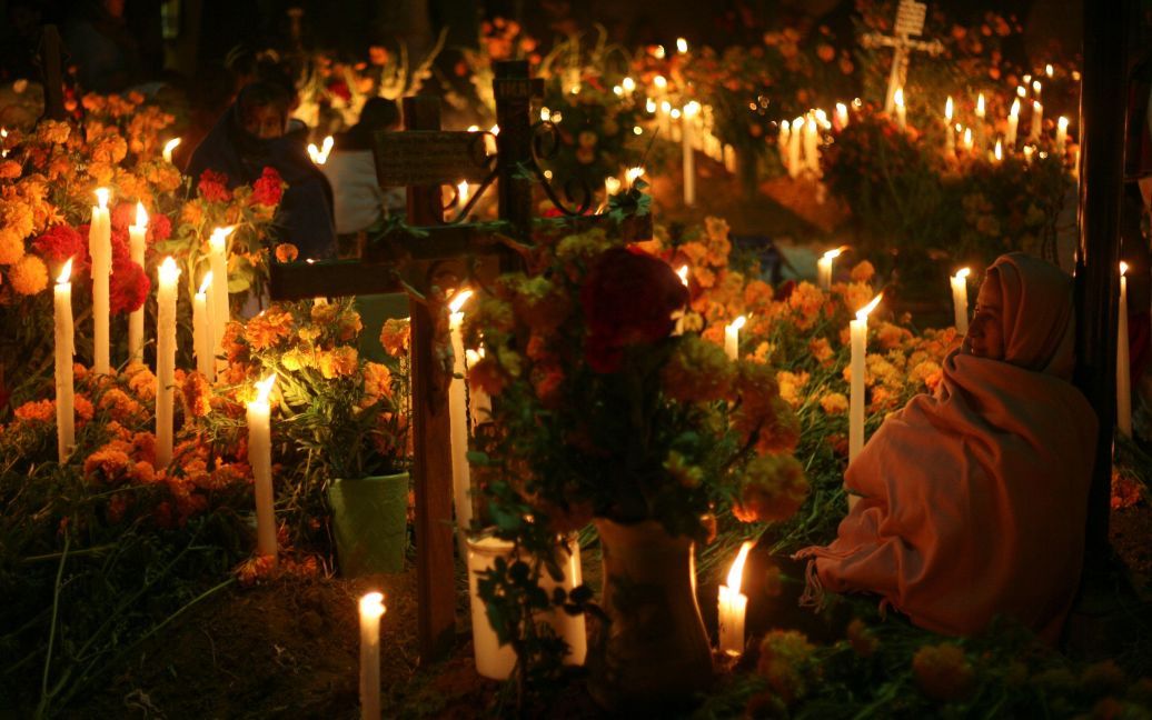 Жінка сидить поруч з могилою на День мертвих, згадуючи своїх померлих родичів на кладовищі у місті Оахака, Мексика. День мертвих щорічно відзначається 1 і 2 листопада у Мексиці, Гватемалі, Нікарагуа, Сальвадорі та Гондурасі. Вважається, що у ці дні душі померлих відвідують свої земні домівки. / © Reuters