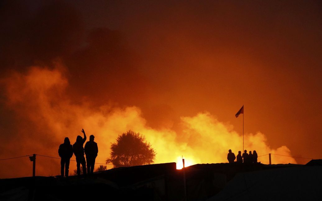 Мигранты собираются возле огня на второй день их эвакуации в приемные центры во Франции, в рамках демонтажа лагеря под названием &laquo;Джунгли&raquo; в Кале. / © Reuters