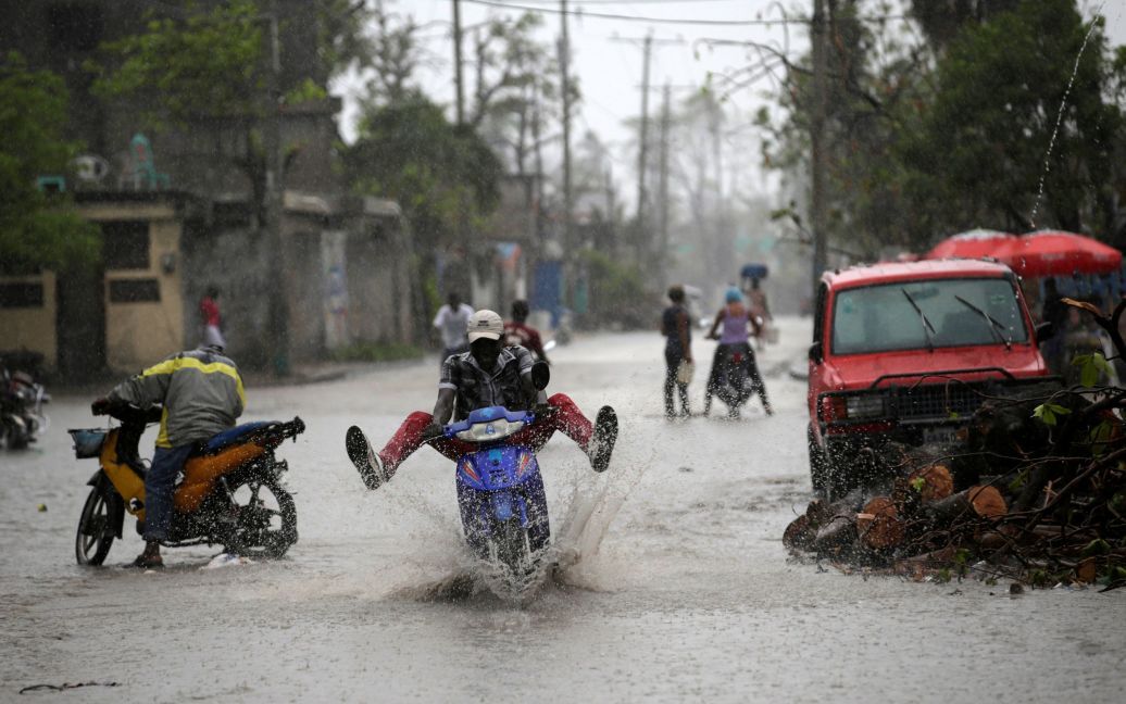 Человек на мотоцикле едет по затопленной улице во время дождя после урагана Мэтью в Ле-Ке, Гаити. / © Reuters