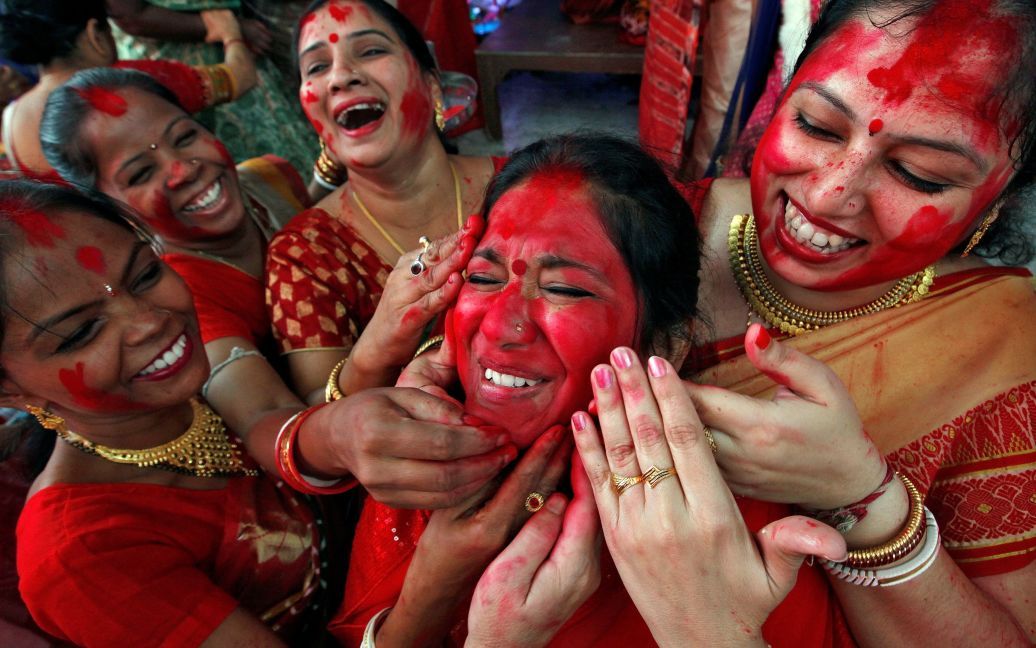 Индийские женщины наносят "сіндур", красный порошок, на лицо женщины после поклонения идолу индусской богини Дурги в последний день фестиваля Дурга Пуджа в Чандігарху, Индия. / © Reuters