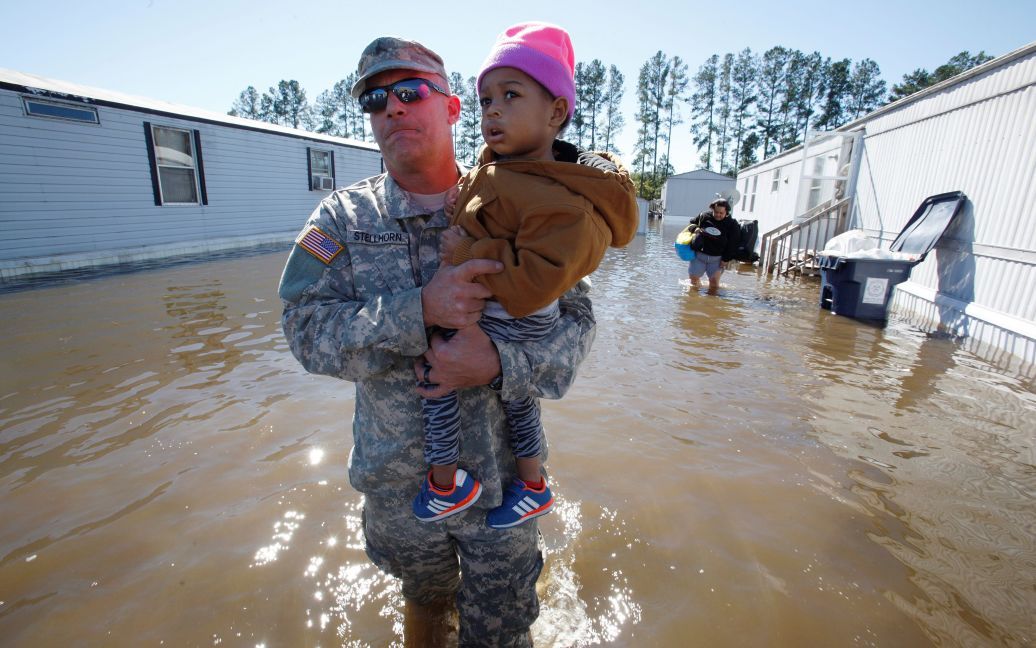 Боец Национальной гвардии США несет двухлетнюю девочку через паводковые воды во время операции по спасению обитателей парка мобильных домов в городе Ламбертон, которое пострадало в результате урагана &ldquo;Мэтью&rdquo;. / © Reuters