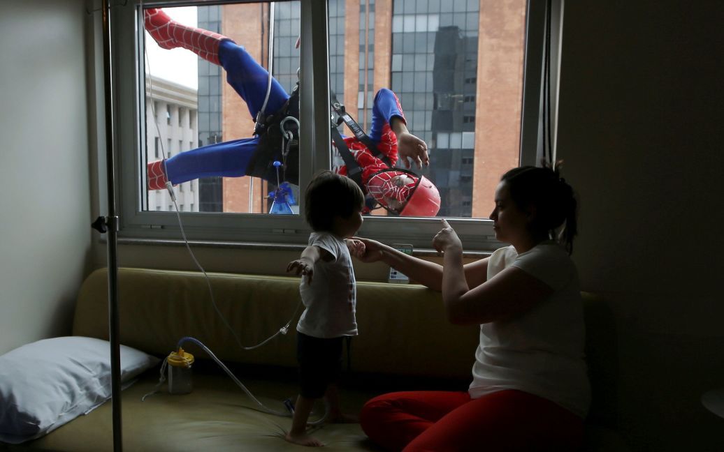Мужчина, одетый как Человек-паук, шутит с маленьким пациентом и его матерью внутри больницы в Сан-Паулу, Бразилия. Мужчины в костюмах чистили стекла детской больницы в рамках Дня защиты детей, который в Бразиліх отмечается 12 октября. / © Reuters