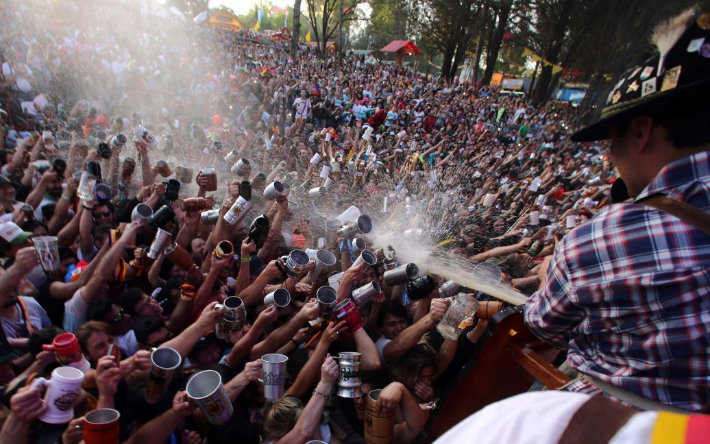 Посетители пытаются заполнить свои кружечки в то время, как пиво распыляется на них из бочки на Октоберфесте в Вилла Генерал Бельграно, Аргентина. / © Reuters