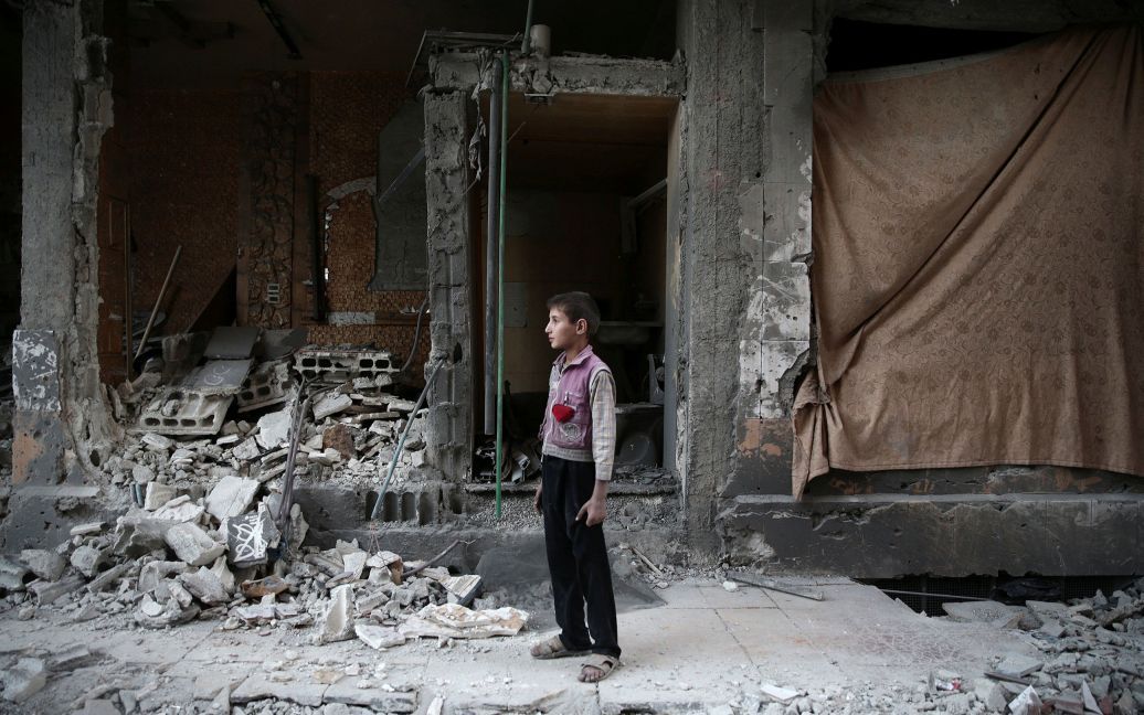 Мальчик стоит возле поврежденного здания в результате авиаудара по контролируемому повстанцами городу Дума близ Дамаска, Сирия. / © Reuters