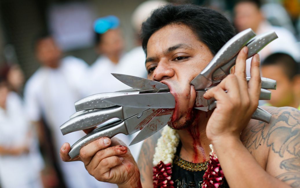 Член китайской общины проколоть с ножами лицом участвует в процессии празднования ежегодного Вегетарианского фестиваля на острове Пхукет, Таиланд. / © Reuters