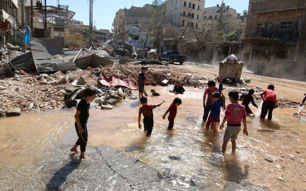 Дети играют в воде с разрыва водопроводной трубы на месте вчерашнего авиаудара в контролируемом повстанцами городе Аль-Мешхед вблизи Алеппо, Сирия. / © Reuters