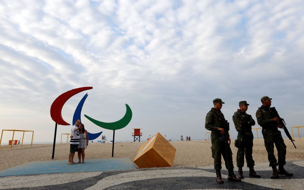 Бразильские солдаты стоят на страже, пока люди делают селфи с паралимпийским символом на пляже Копакабана в Бразилии. / © Reuters