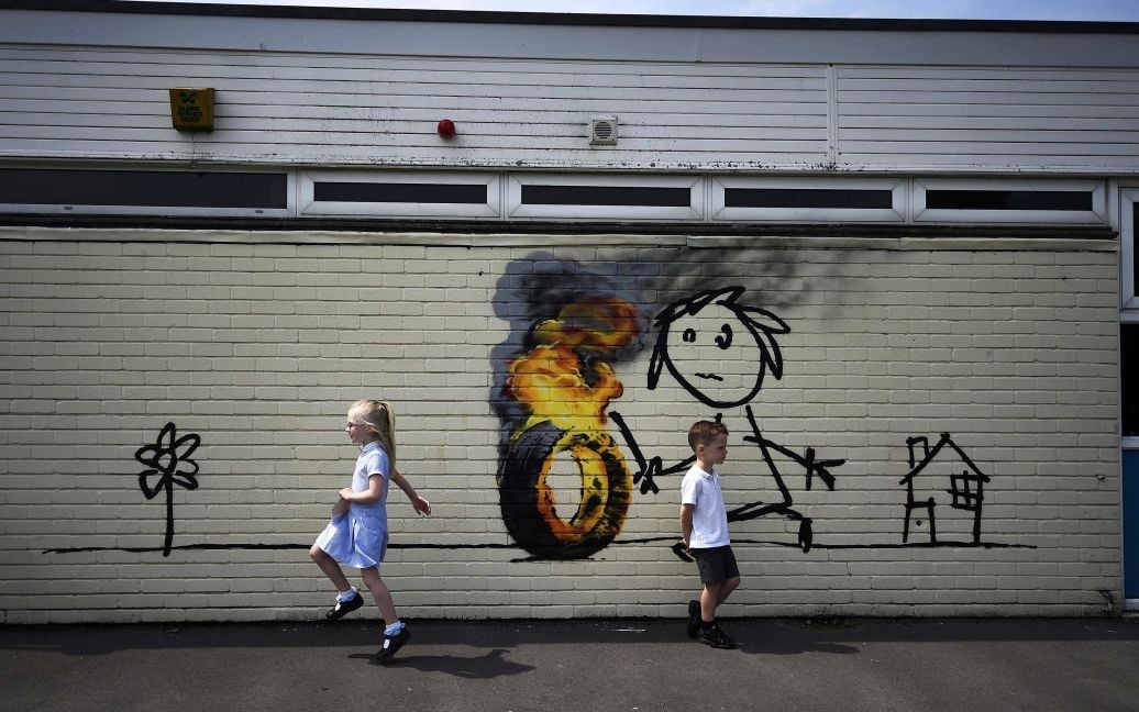 Школьники идут мимо граффити, которое приписывают художнику Бэнкси, нарисованному на внешней стороне классной комнаты начальной школы в Бристоле, Великобритания. / © Reuters