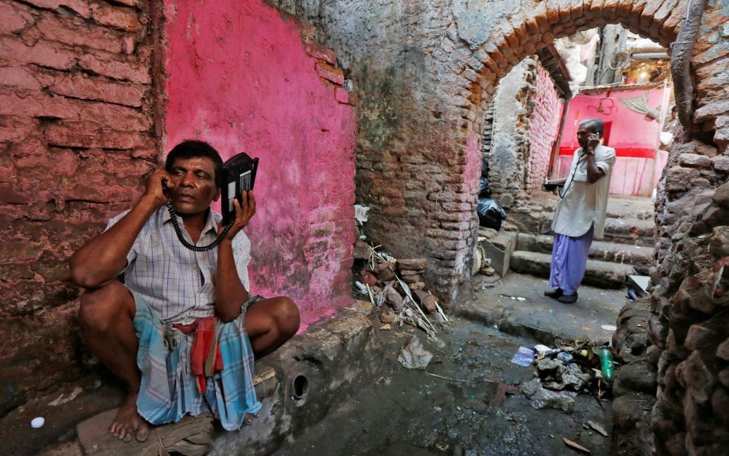 Робітники говорять по мобільних телефонах у провулку за межами місцевої телефонної будки в Калькутті, Індія. / © Reuters