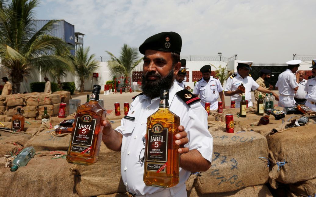 Офіцер з Агентства морської безпеки  Пакистану тримає вилучені пляшки лікеру під час прес-конференції в Карачі, Пакистан. Принаймні 12400 пляшок і банок незаконного лікеру на суму 60 мільйонів пакистанських рупій були у катері, який силовики перехопили у відкритому морі. / © Reuters