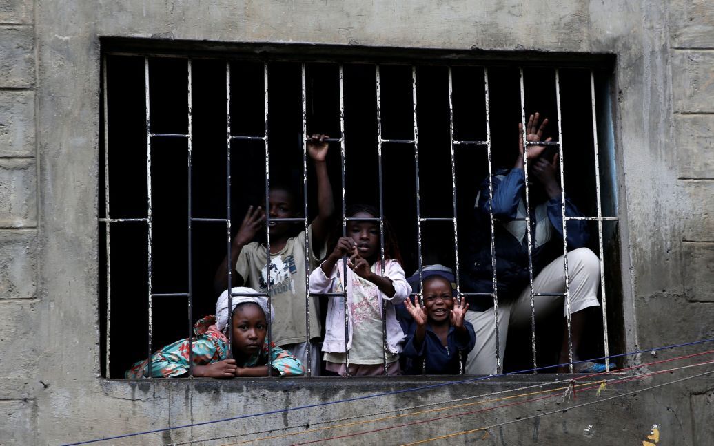 Дети смотрят через решетку, в то время как спасатели ищут жителей, которые могли остаться под обломками шестиэтажного дома, который упал после нескольких дней сильного дождя в Найроби, Кения. / © Reuters
