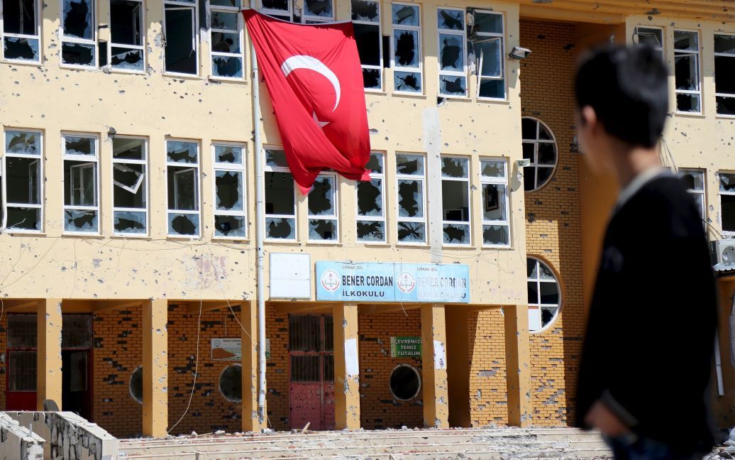 Хлопчик стоїть перед початковою школою, яка була пошкоджена під час операцій із забезпечення безпеки під час зіткнень між турецькими силами безпеки і курдськими бойовиками, в південно-східній частині міста Іділ, Туреччина. / © Reuters