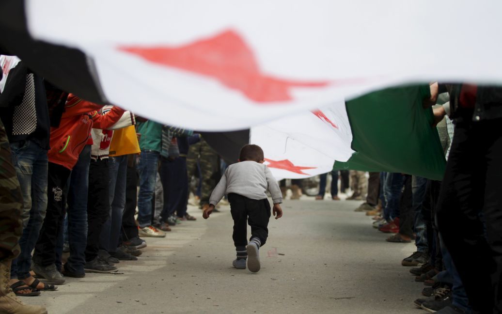 Мальчик ходит под флагом оппозиции во время антиправительственного протеста в контролируемом повстанцами районе города Маарет аль-Нуман в провинции Идлиб, Сирия. / © Reuters