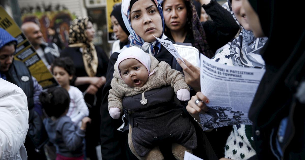 Афганская мигрантка несет своего ребенка рядом с активистами и студентами, которые принимают участие в акции протеста против недавнего закрытия границы через Балканы, в Афинах, Греция. / © Reuters