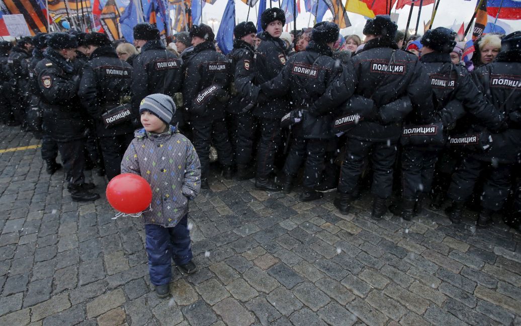 Хлопчик стоїть перед російськими поліцейськими під час святкового концерту з нагоди другої річниці анексії Криму Росією на Красній площі в центрі Москви. / © Reuters