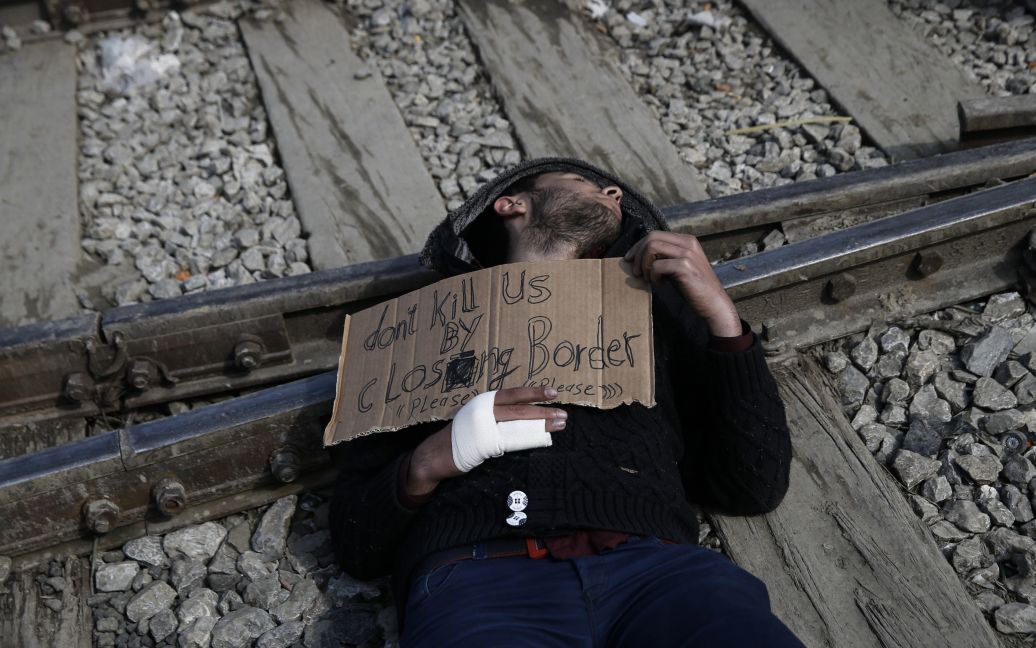 Сирійський біженець лежить на залізничних коліях з плакатом, що вимагає відкрити для них кордони в ЄС. Акція протесту відбулася у наметовому таборі на греко-македонському кордоні поблизу села Ідоменей, Греція. / © Reuters
