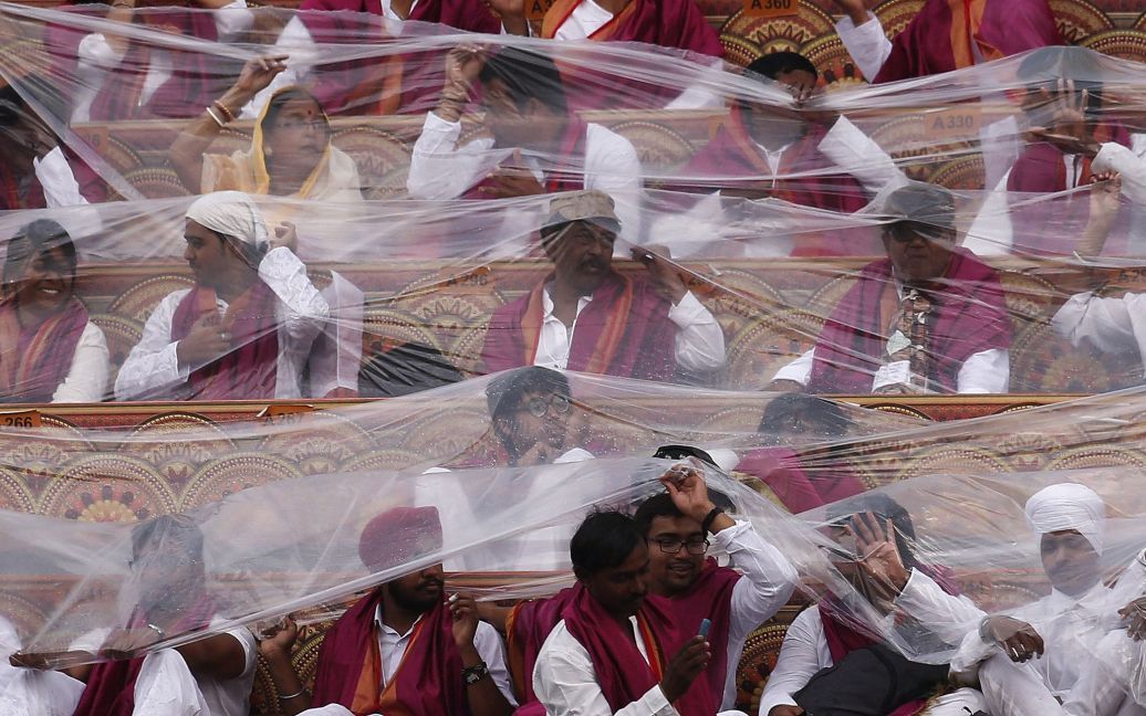 Участники Всемирного фестиваля культуры в индийском Нью-Дели прикрываются пластиковыми листами от дождя. / © Reuters
