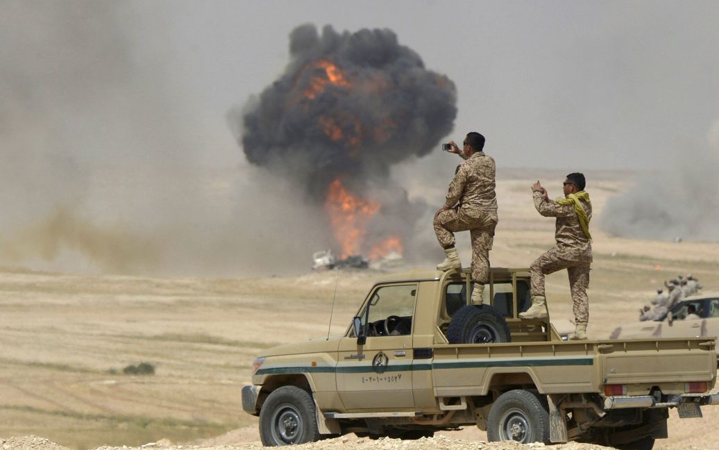 Солдаты фотографируют, как поднимаются пламя и дым в результате авиаудара во время учений недалеко от границы Саудовской Аравии с Ираком. / © Reuters