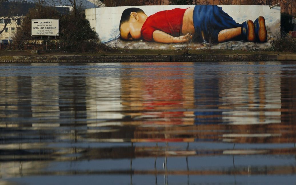 Величезне графіті, яке зображує загиблого маленького біженця Айлана Курді, видно на стіні на березі річки Майн, недалеко від штаб-квартири Європейського центрального банку у Франкфурті, Німеччина. / © Reuters