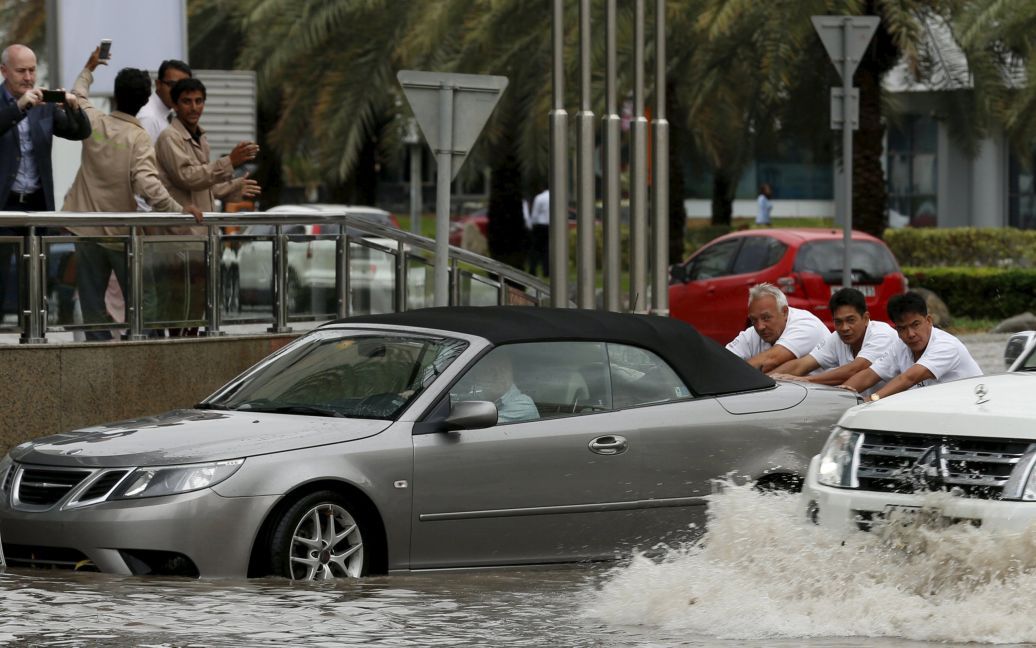 Люди толкают машину сквозь паводковые воды во время шторма в Дубае, ОАЭ. / © Reuters